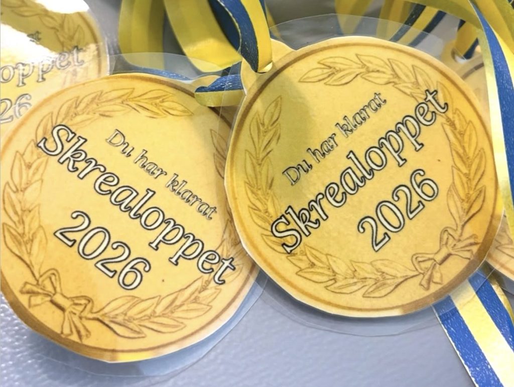Närbild på flera guldfärgade medaljer med texten 'Du har klarat Skrealoppet 2026' omgivna av en lagerkrans, hängande i blågula band.